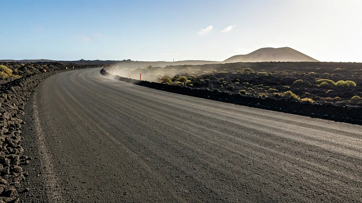 Image of a road under construction with dirt sections in a Canarian landscape.