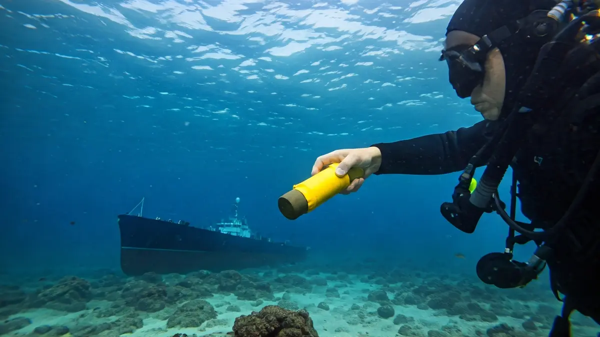Imagen de un buzo manipulando un artefacto explosivo simulado bajo el agua durante un ejercicio de seguridad marítima.