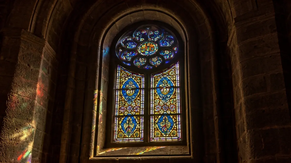 Imagen de una vidriera de colores en el interior de una iglesia antigua, con la luz del sol atravesándola.