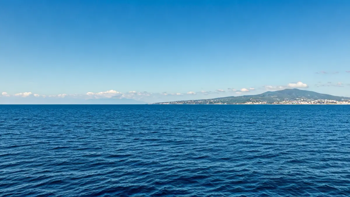 Imagen de un barco de carga navegando cerca de una costa volcánica.