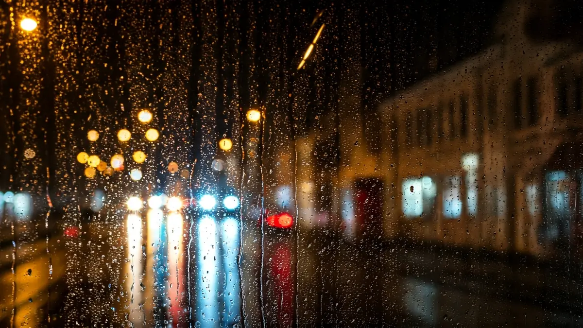 Image of a bus windshield with reflections of emergency lights on a rainy night.
