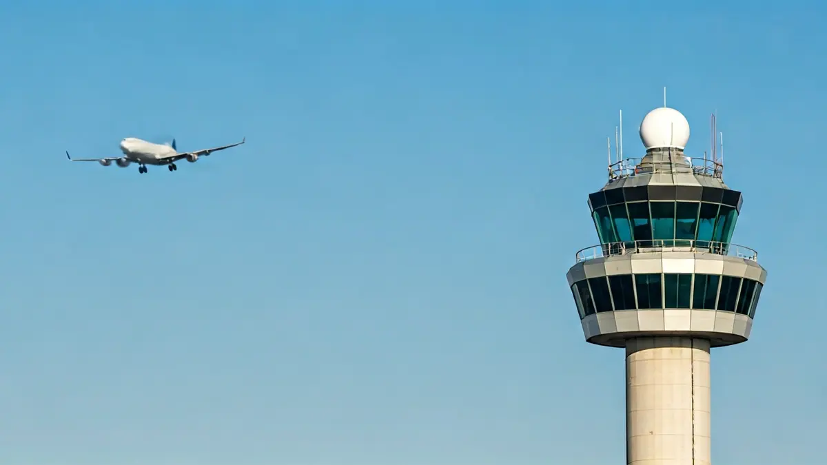 Imagen genérica de una torre de control de aeropuerto con un avión despegando al fondo.