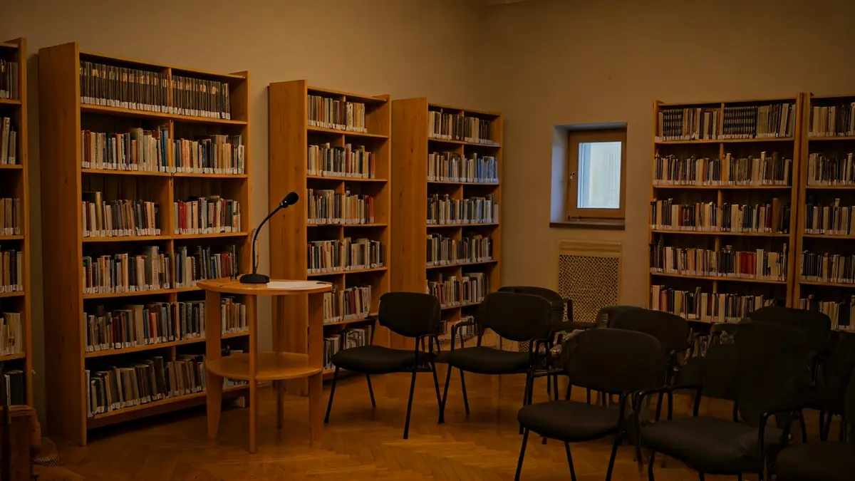 Imagen genérica de un salón de actos o biblioteca con un micrófono y sillas vacías, iluminado cálidamente.