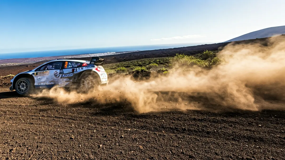 Imagen de un neumático de coche de rally levantando polvo en una pista de tierra con el paisaje volcánico de La Palma de fondo.