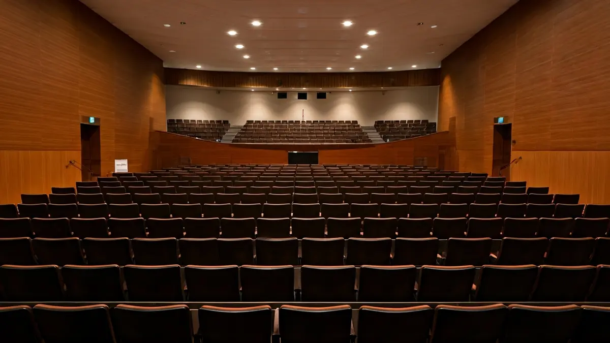 Imagen de un auditorio moderno con asientos vacíos y un micrófono en el escenario, listo para una reunión comunitaria.