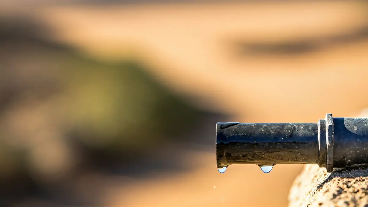 Imagen de una tubería con una fuga de agua en un entorno árido.