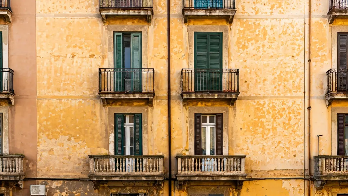 Fachada de un edificio de viviendas con signos de desgaste, en un entorno urbano mediterráneo.