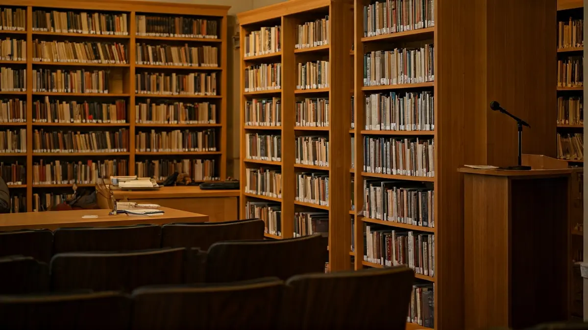 Imagen genérica de un interior de biblioteca con estanterías de madera y un podio con micrófono, iluminado con luz cálida.