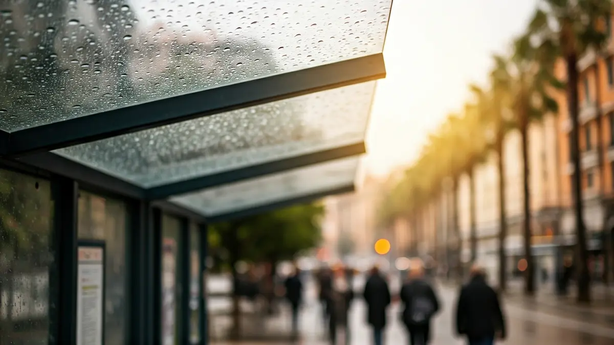 Modern bus stop shelter with transparent roof and raindrops, blurred urban background with palm trees.