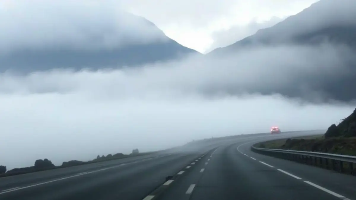 Imagen de una carretera cubierta por una densa niebla, con poca visibilidad y luces de vehículos borrosas.
