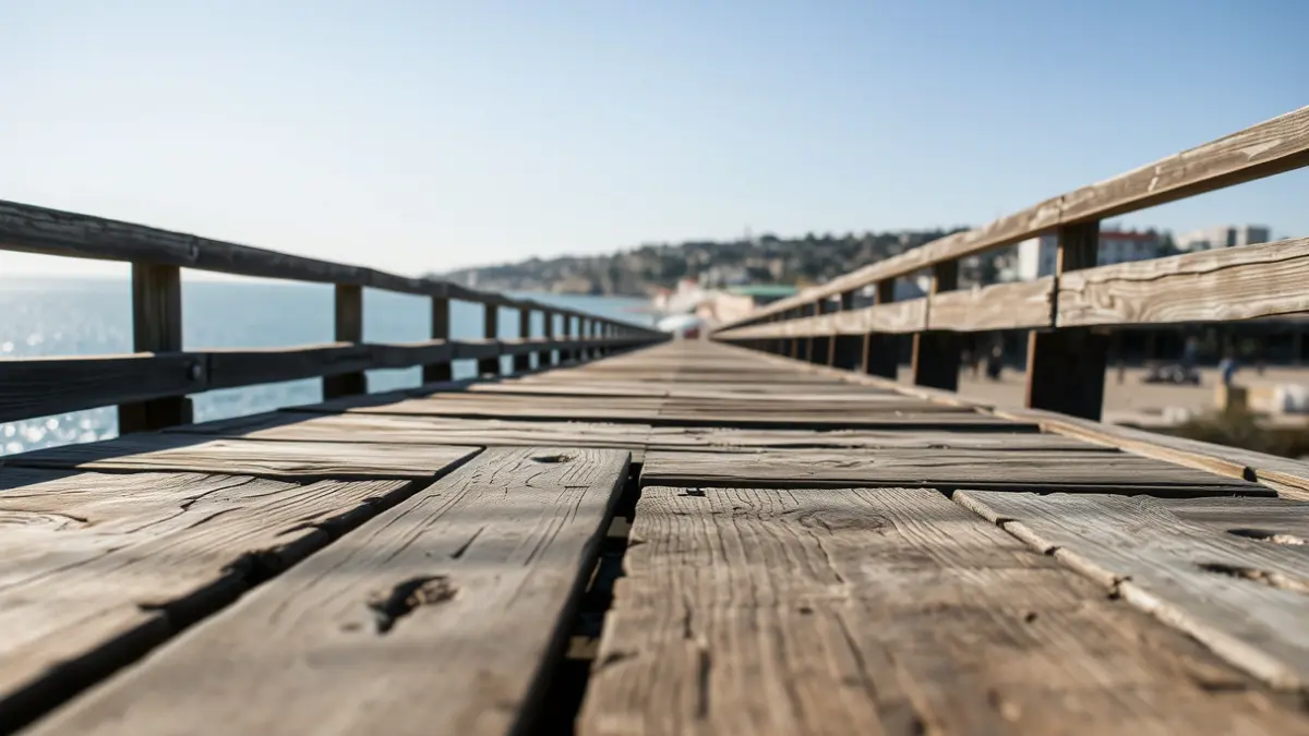 Paseo marítimo de madera deteriorado con soportes expuestos y el océano de fondo.