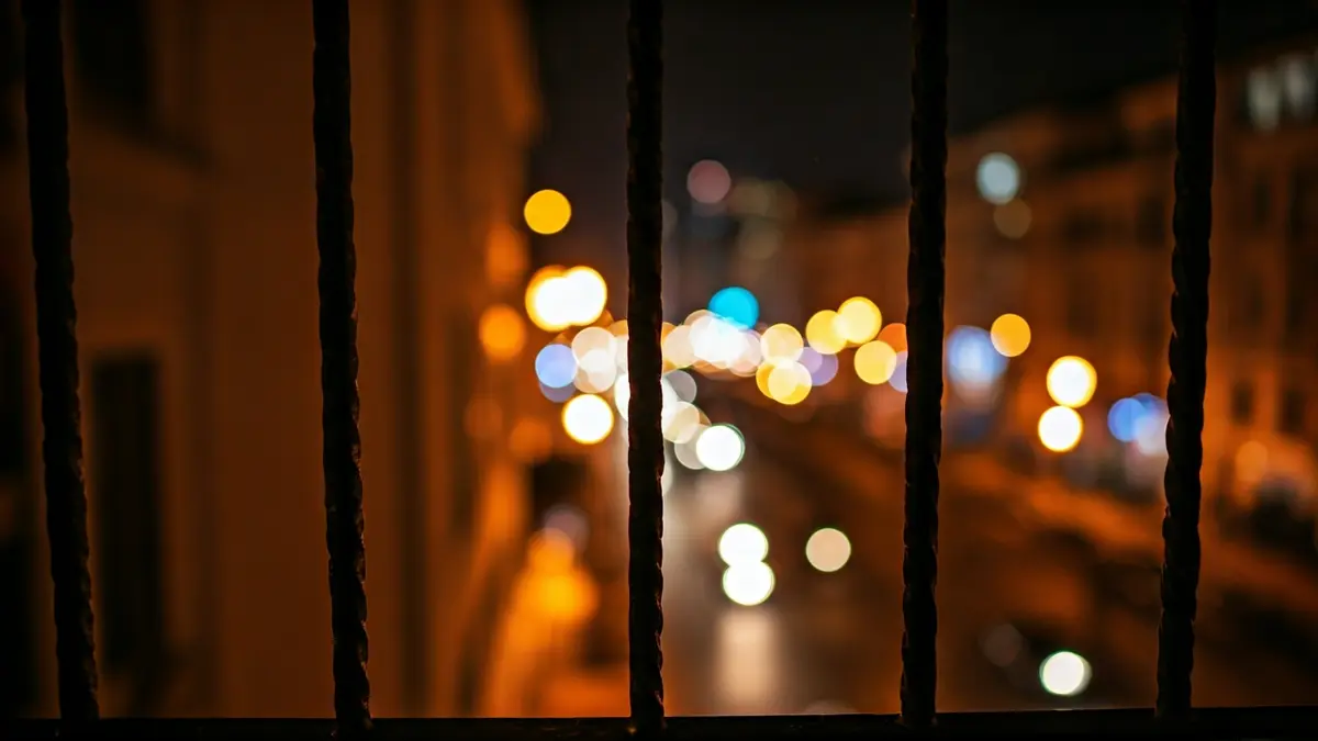 Imagen de un balcón de hotel por la noche, con luces borrosas de la ciudad al fondo.