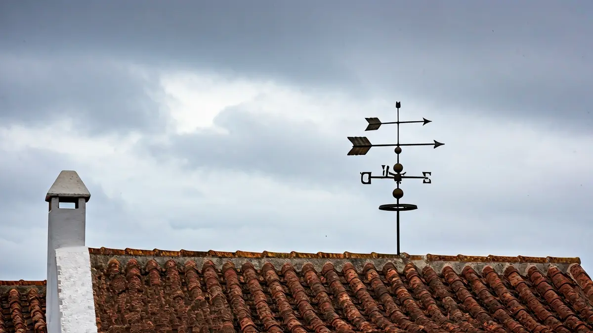Imagen genérica de una veleta en un tejado bajo un cielo nublado con lluvia ligera.