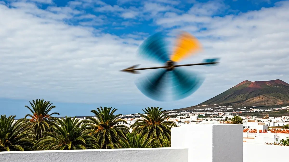 Imagen genérica de una veleta girando con fuerza en un tejado, con palmeras y paisaje volcánico de fondo, indicando vientos fuertes en Canarias.