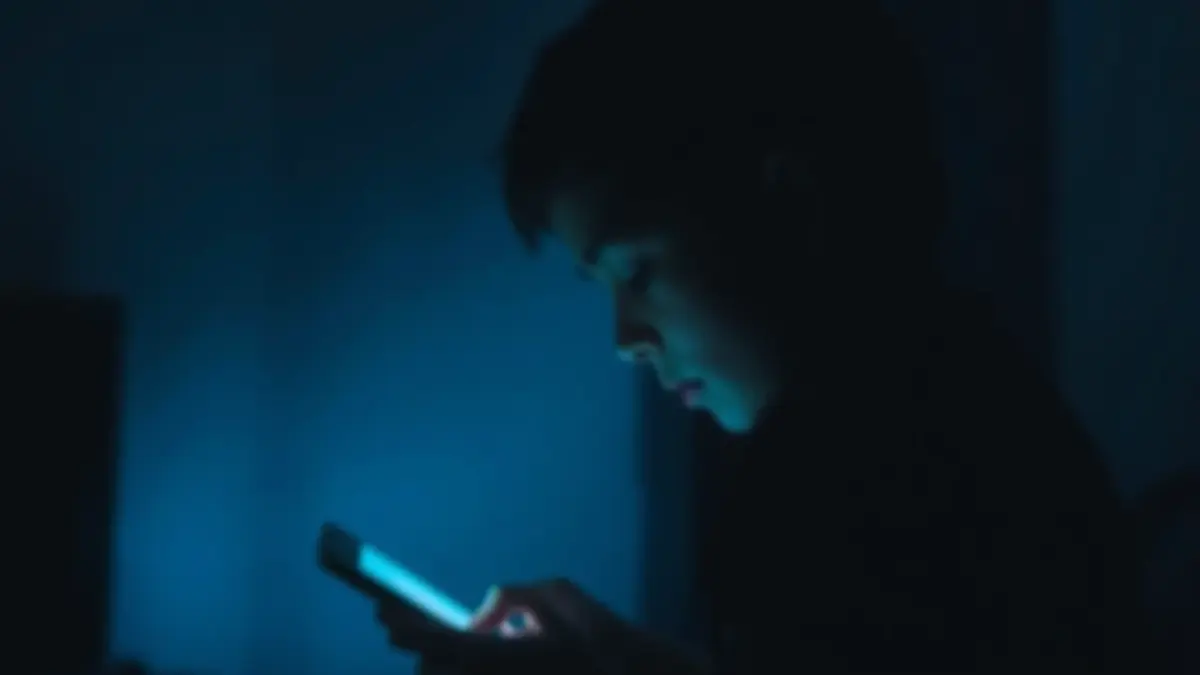 Generic image of a teenager using a mobile phone in a dark environment, symbolizing isolation.