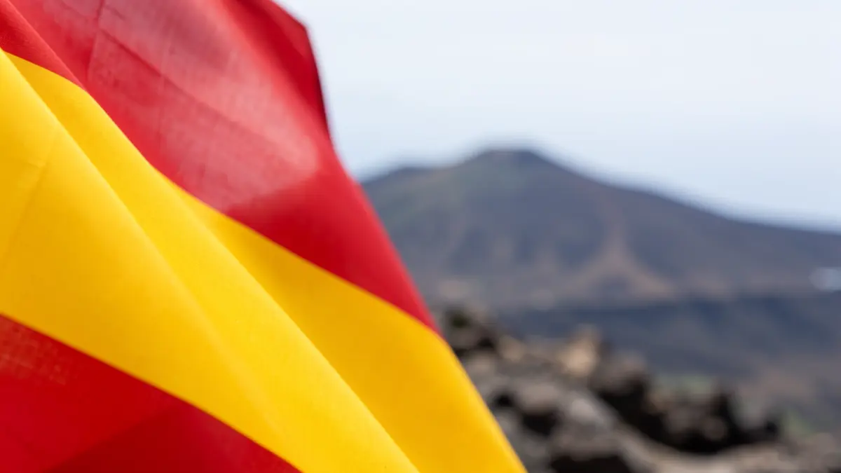 Detalle de la bandera de España con el paisaje volcánico de Canarias al fondo.