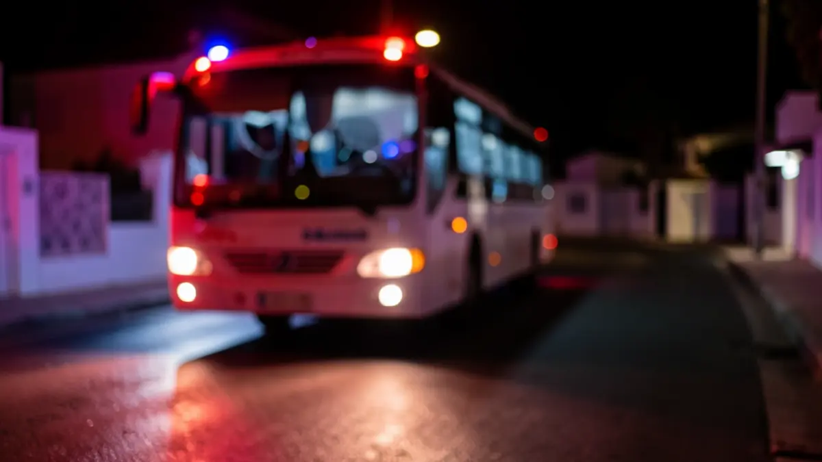 Imagen genérica de una guagua con cristales rotos por la noche, iluminada por luces de emergencia.
