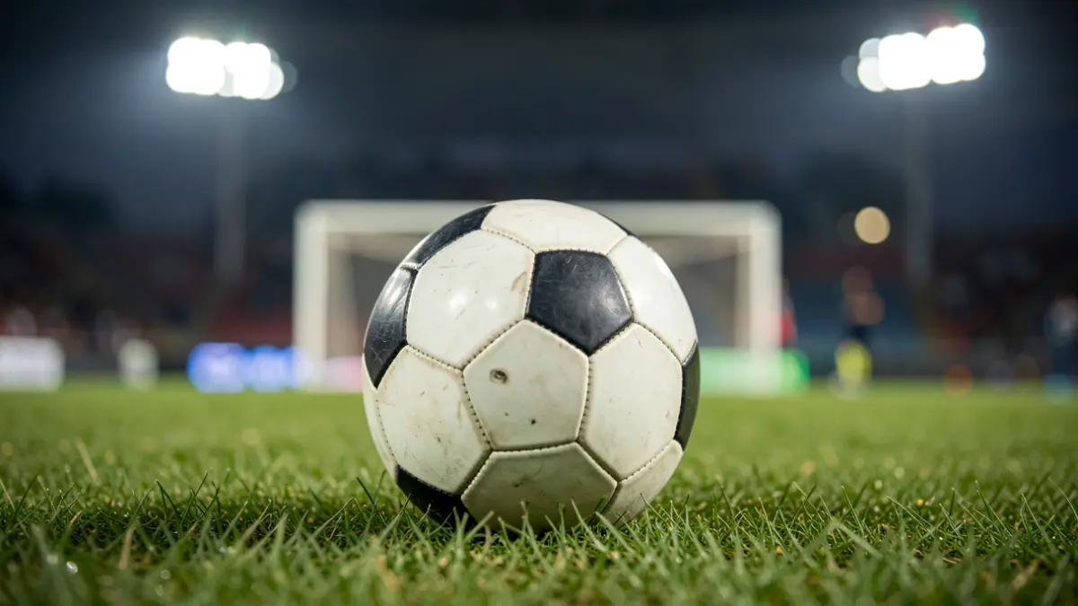 Generic image of a soccer ball on grass with a blurred stadium in the background.