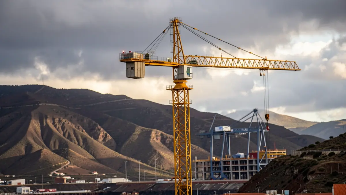 Construction crane in a volcanic landscape of the Canary Islands with a port structure under construction.