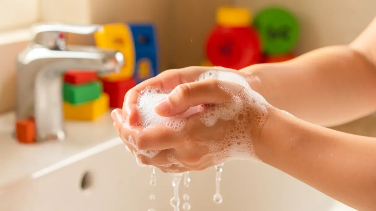 Imagen genérica de manos lavándose con jabón y agua en un entorno infantil.