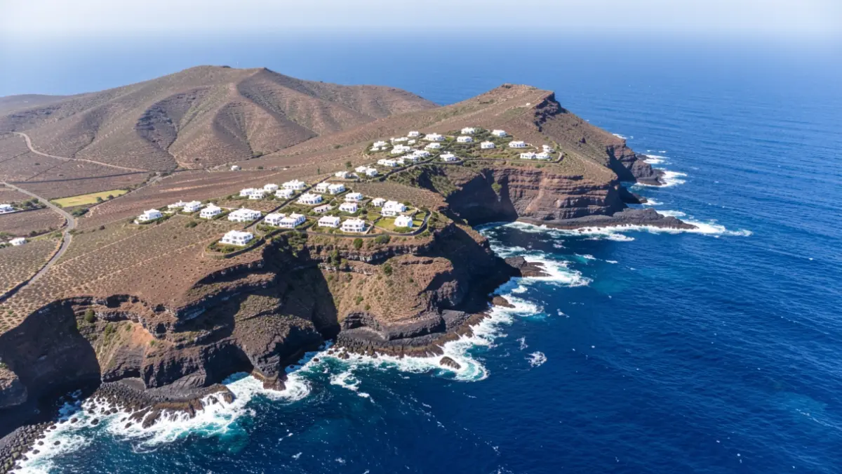 Aerial view of a volcanic island coastline in the Canary Islands, with scattered white houses and blue ocean.