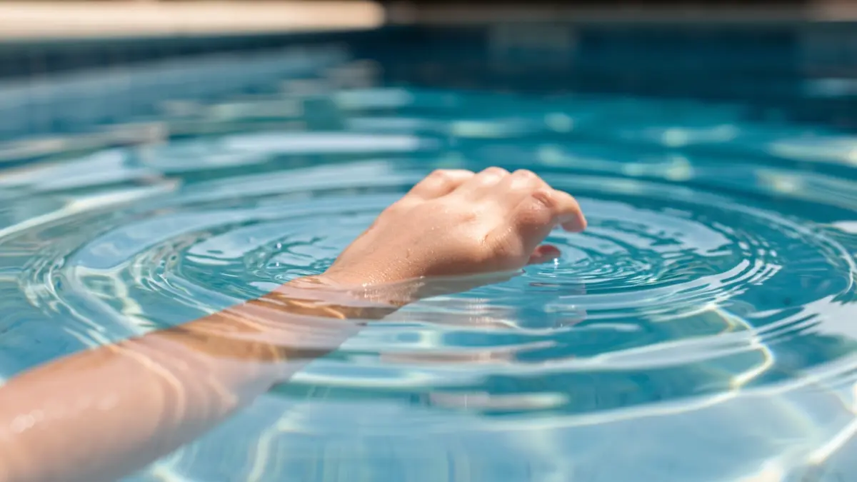 Mano de un bebé flotando en el agua de una piscina con signos de ahogamiento.