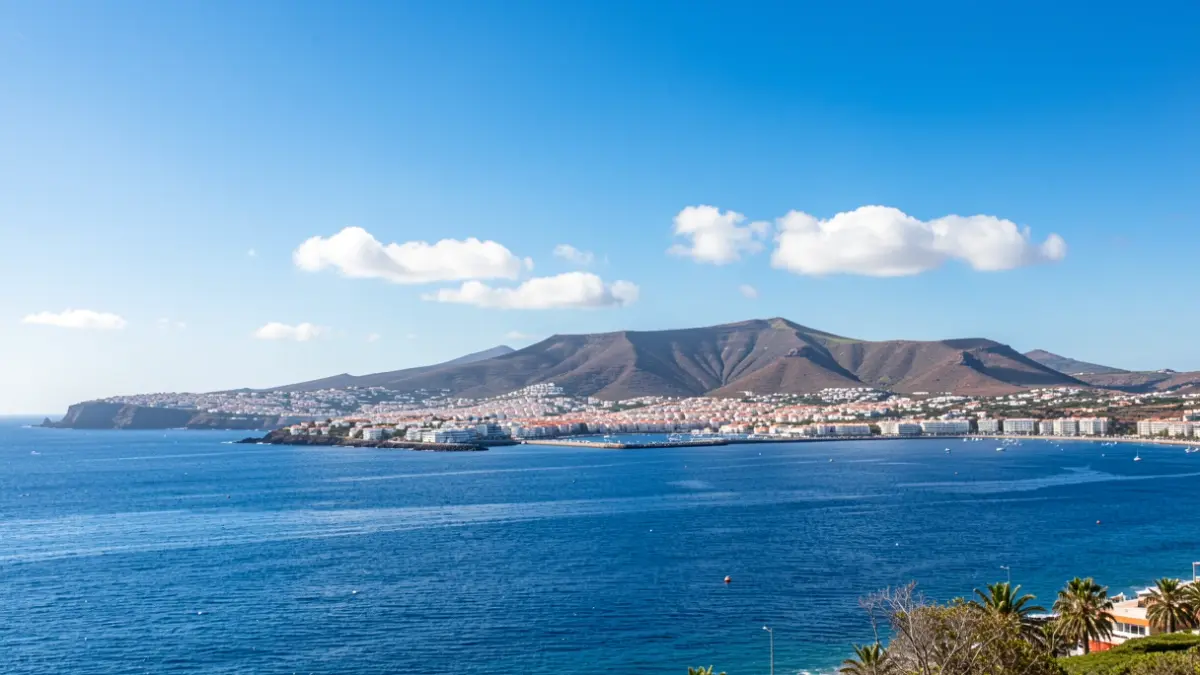 Sunny sky over a coastal town in the Canary Islands with volcanic hills in the background.