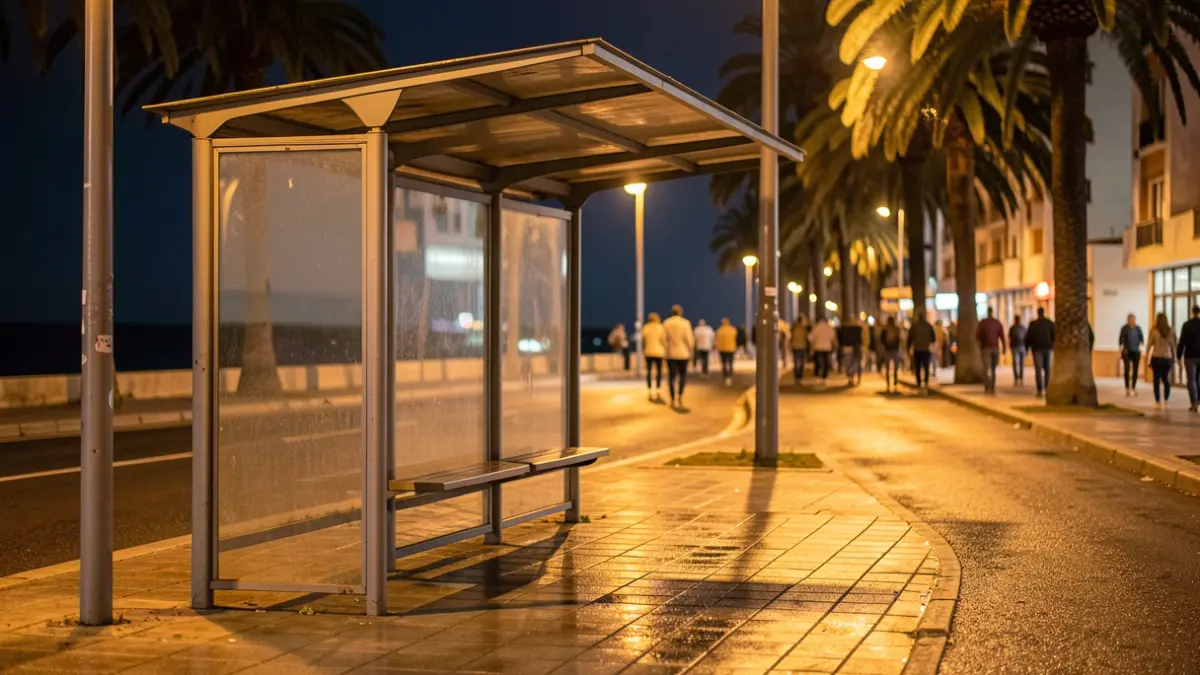 Empty bus stop at night in Las Palmas de Gran Canaria, with palm trees and the sea in the background.