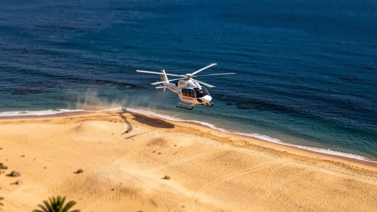 Imagen aérea de una playa de Gran Canaria con un helicóptero de rescate sobrevolando la zona.
