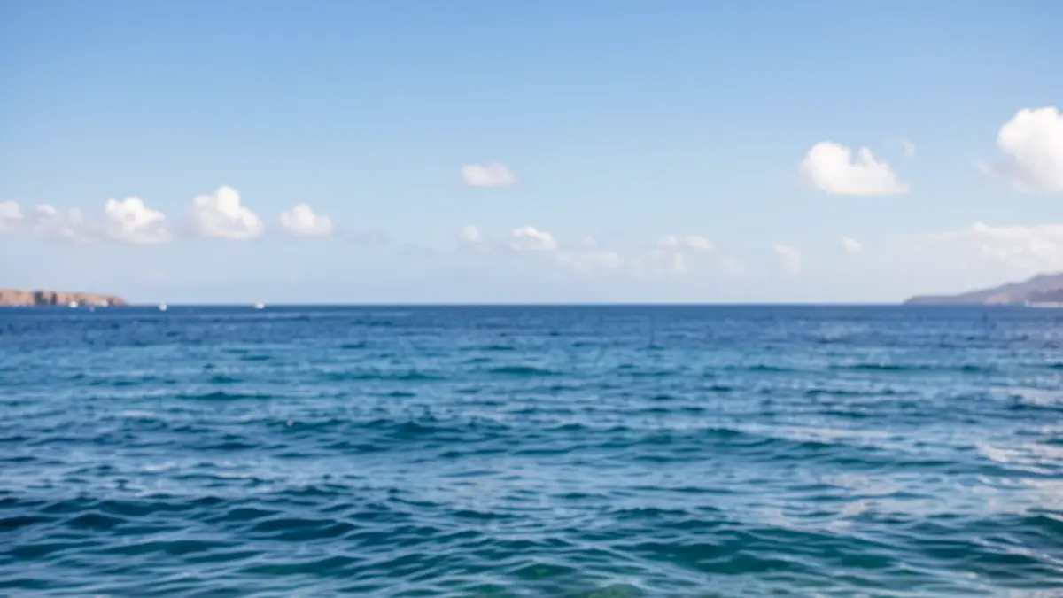 Cielo azul despejado con algunas nubes blancas sobre el mar tranquilo.