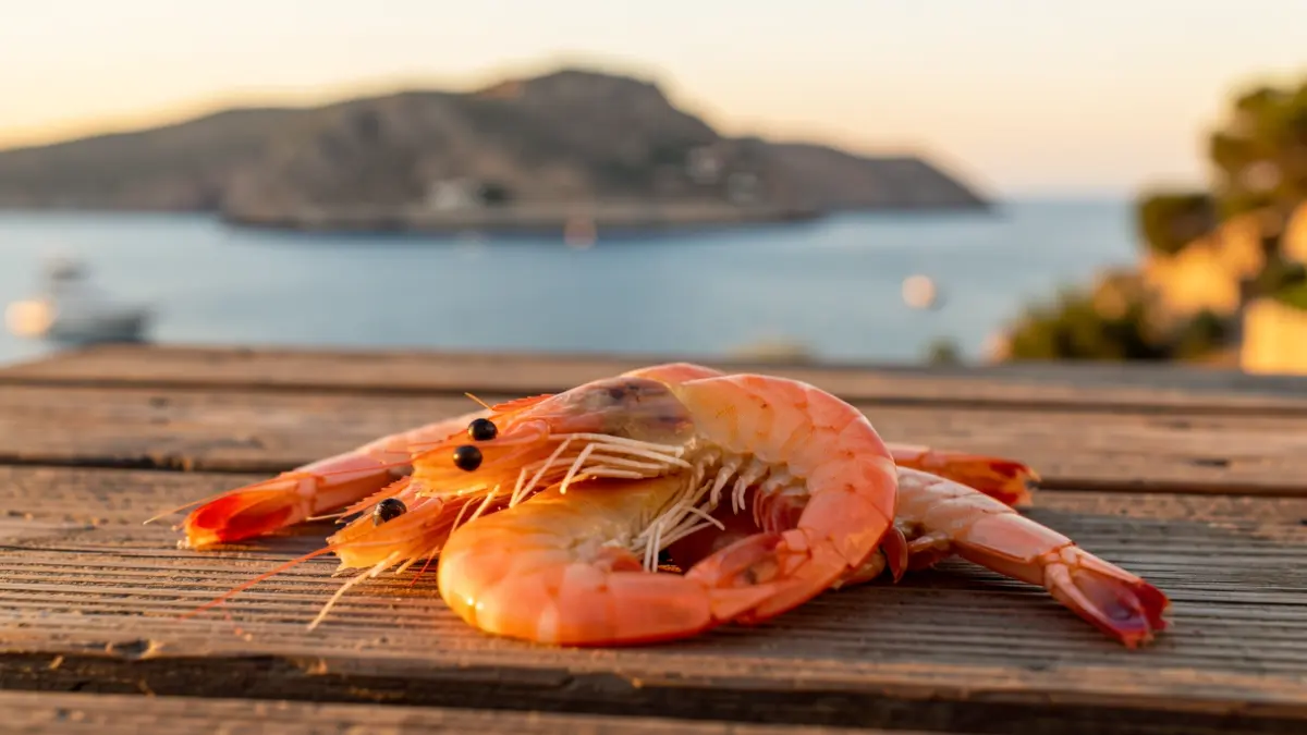 Image of fresh shrimp on a wooden table with the coastal landscape of Bajamar in the background.