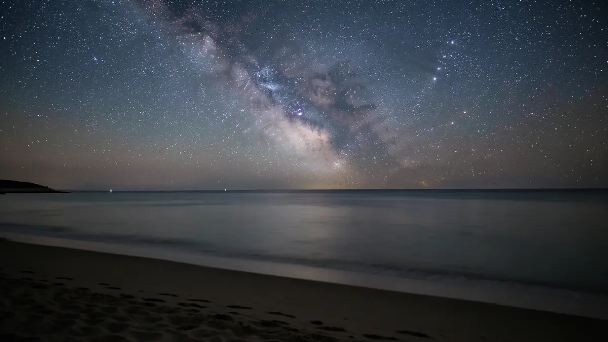 Starry night sky over a dark beach.