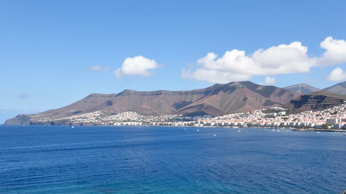 Sunny sky over a coastal town in the Canary Islands with volcanic hills in the background.