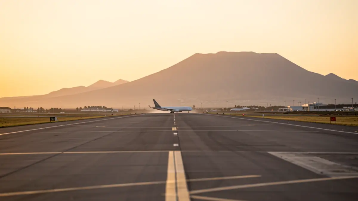 Image of an airport runway at sunset with an aircraft silhouette in the background.