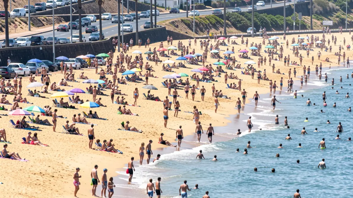 Image of Las Teresitas beach crowded with people during a heatwave, with traffic on the access road.