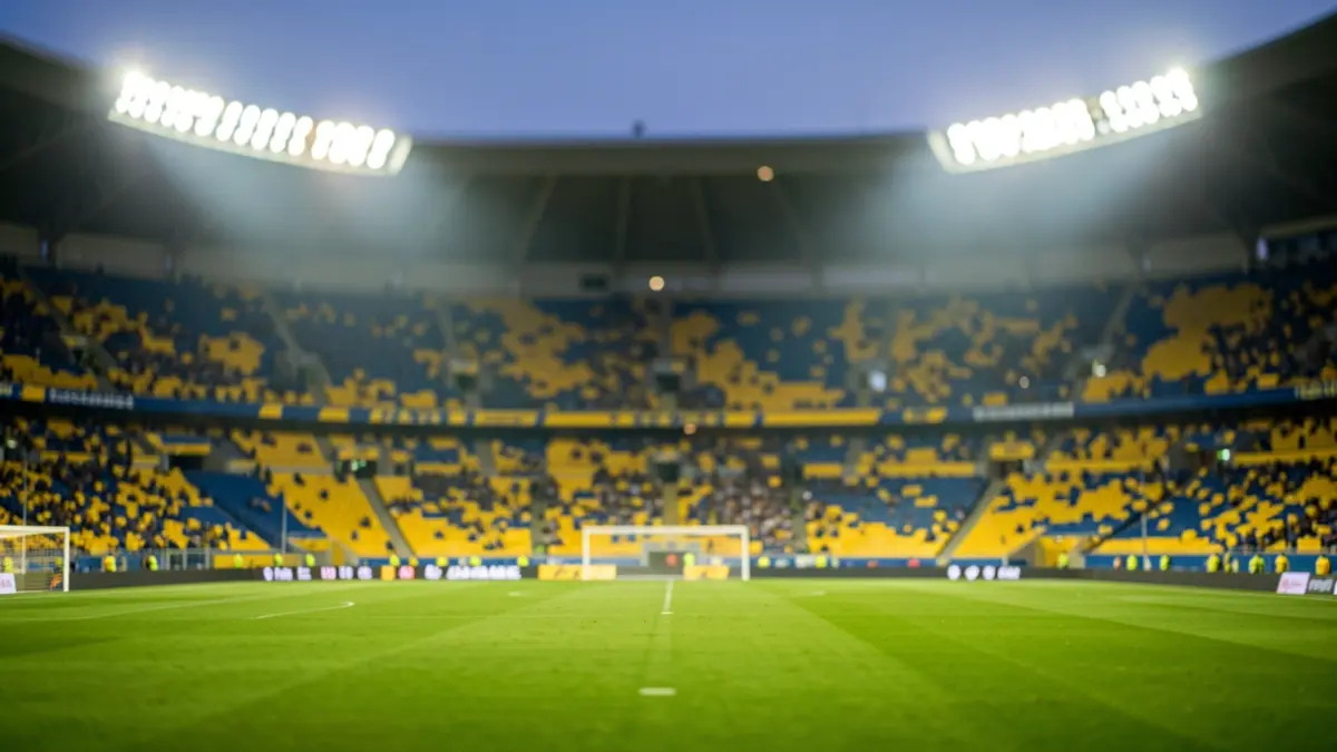 Generic image of a football stadium with lights on and empty stands, featuring yellow and blue colors.