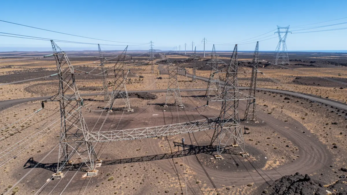 Vista aérea de antiguos postes eléctricos siendo desmantelados en Fuerteventura, con una nueva línea eléctrica en la distancia.