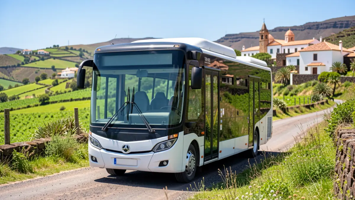 Hybrid bus-taxi vehicle on a rural road in Gran Canaria with traditional architecture in the background.